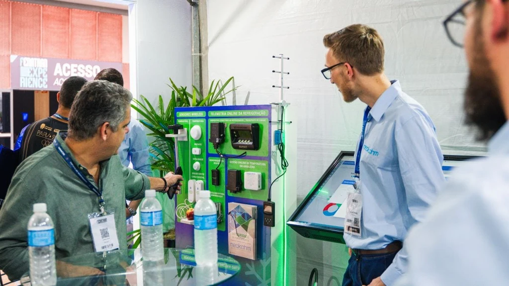 Integrante da Neokohm observa visitante no painel de sensores wireless e telemetria online da refrigeração, no estande da FENATRAN 2024