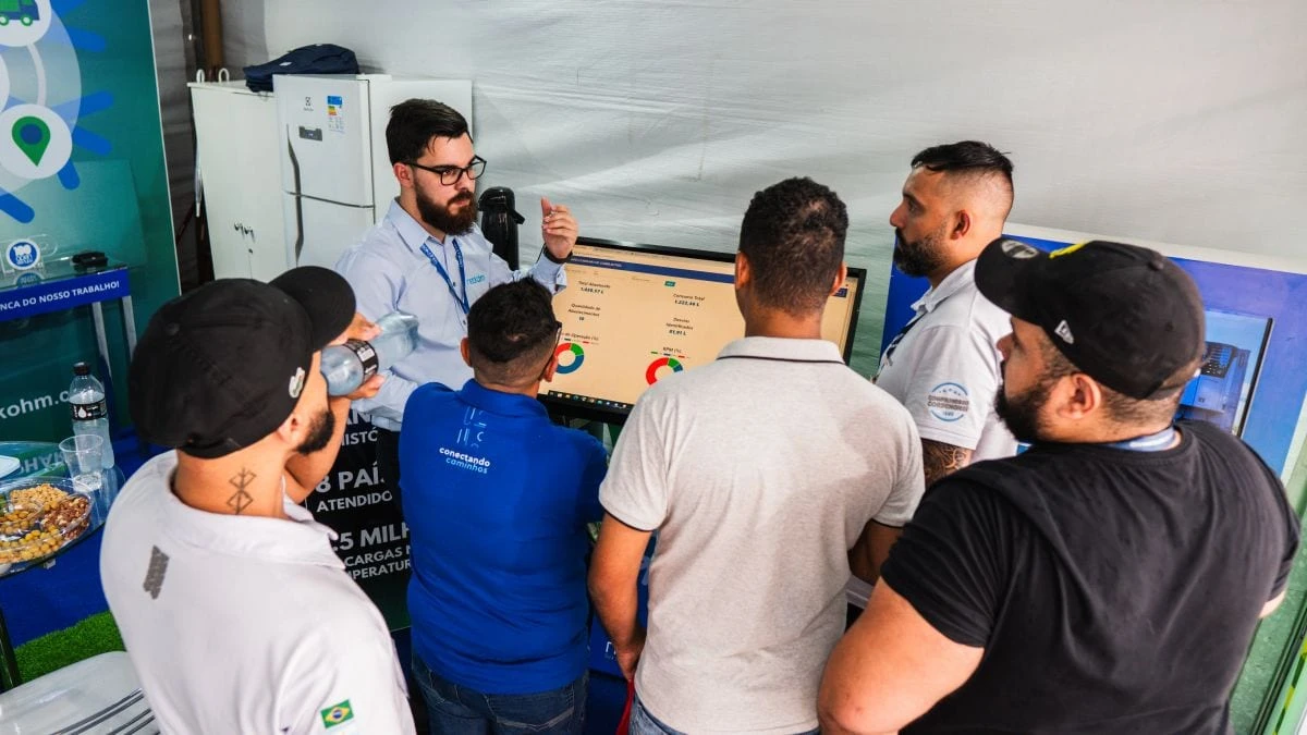 Homem de óculos e camisa azul-clara explica a um grupo de visitantes uma tela com indicadores de abastecimento e gráficos de rosca