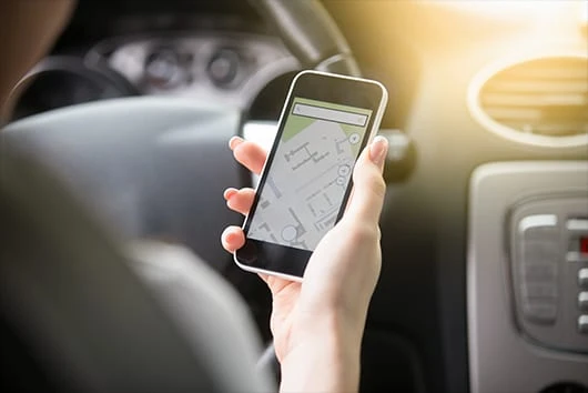 Mão segura um smartphone com um mapa aberto na tela, dentro de um carro, com o volante e o painel desfocados ao fundo