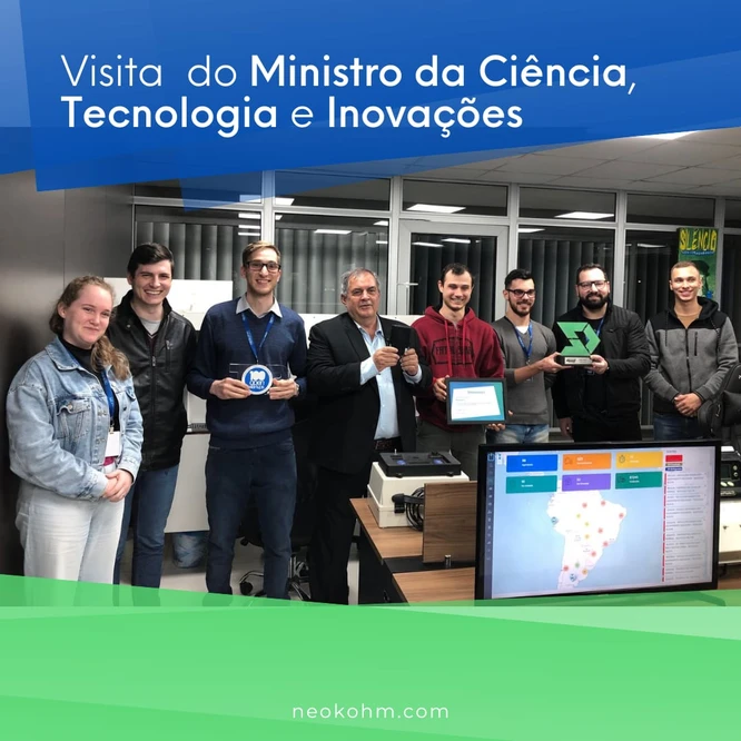 Oito pessoas, entre elas um homem de terno, posam com troféu, selo e certificado; à frente, monitor exibe painel com mapa da América do Sul.